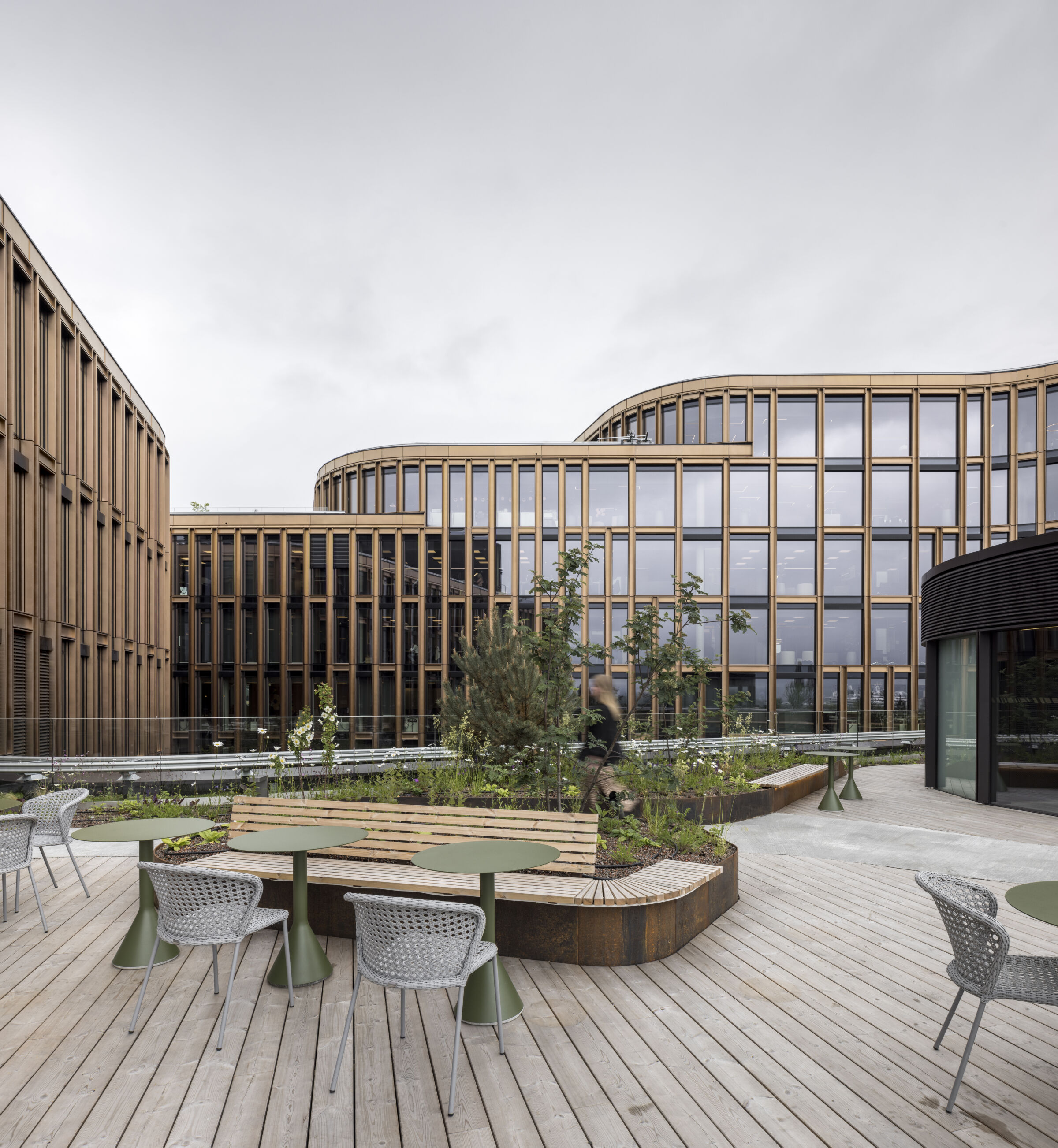curved wood facade panels | glass windows | light wood decking | green metal outdoor tables | woven gray chairs | curved wood bench